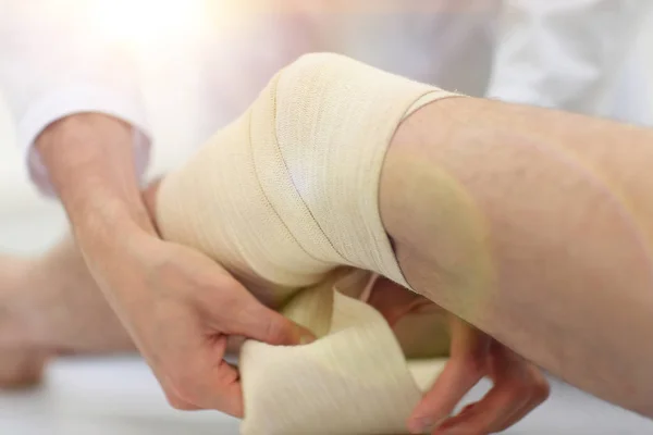 Nahaufnahme. Arzt bandagiert ein Bein des Patienten — Stockfoto