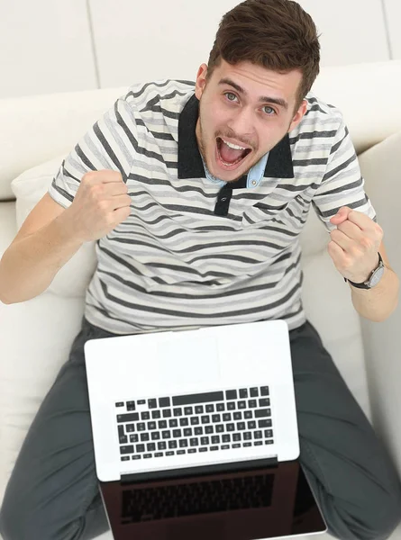 Blick von oben. Jubelnder junger Mann mit Laptop auf der Couch — Stockfoto