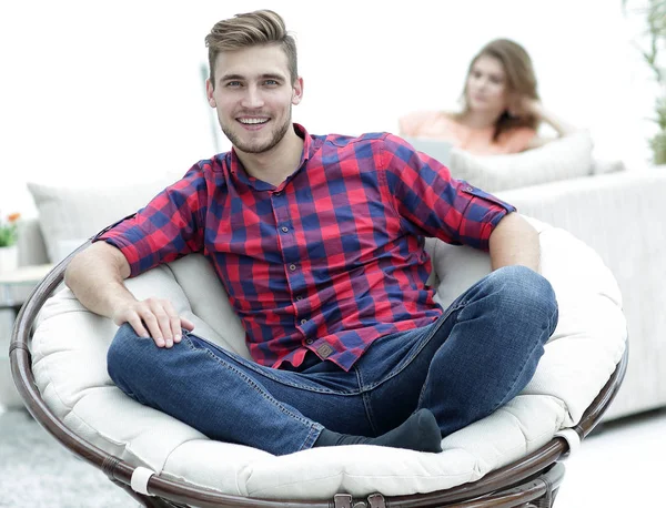 Современный молодой человек, сидящий в большом круглом кресле на размытом фоне — стоковое фото