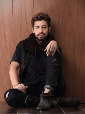 Tuğla duvarın yanında oturan yakışıklı olgun adam. Erkek modası.