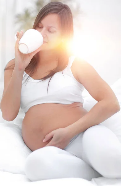 Gelukkig zwangere vrouw consumptiemelk zit in de woonkamer. — Stockfoto