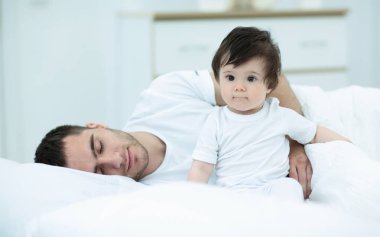 Küçük bir çocuk babası ile evde yatakta oturuyor