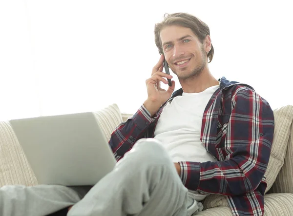 Серйозний молодий чоловік з ноутбуком розмовляє на мобільному телефоні — стокове фото