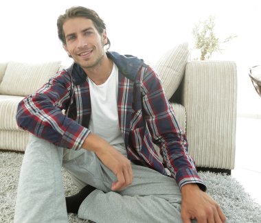 Kendine güvenen adam rahat bir oturma odasında halı üzerinde oturan.