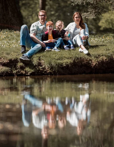 Gelukkig gezin van vier zittend op het gras op het meer — Stockfoto
