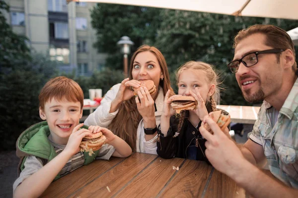 Rodziny głodny jedzenie hamburgerów, siedzi przy stole w restauracji typu fast food — Zdjęcie stockowe