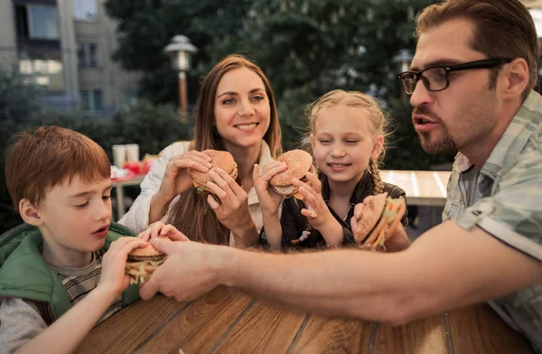 Hungry family eating hamburgers, sitting at a table in a fast food restaurant — Stock Photo, Image