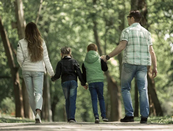 Bakifrån. familj med två barn gå hand i hand i parken. — Stockfoto