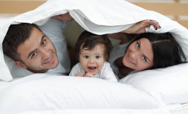 mutlu bir aile kameraya bakarken bir yorgan altında poz