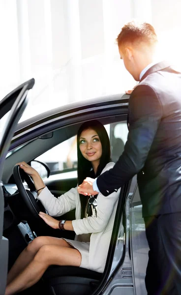 Jovem mulher recebe a chave e sorrindo, sentado em um carro novo no showroom . — Fotografia de Stock