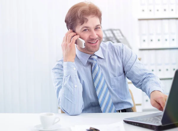 Knappe zakenman zit aan Bureau en praten op een mobiele telefoon — Stockfoto