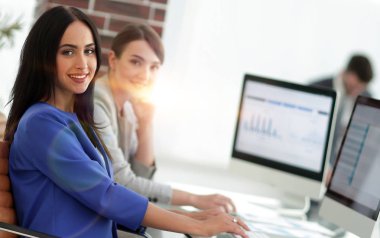 Kameraya bakarak ve oturma işyerinde gülümseyen genç kadın