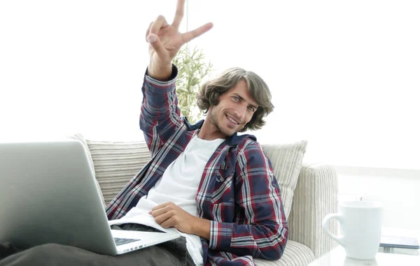 Mutlu adam kanepede oturan ve elini kazanan bir jest gösterilen dizüstü bilgisayar ile — Stok fotoğraf