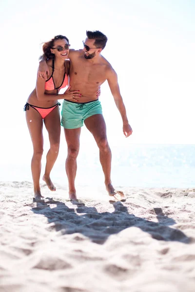 Joven pareja feliz corriendo juntos entre una playa en un día soleado — Foto de Stock