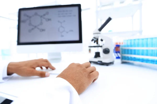 A scientist uses a computer and a microscope — Stock Photo, Image