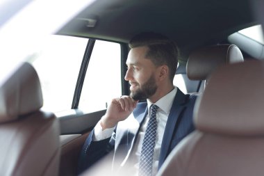 Bir arabanın arka koltuğunda oturan gülümseyen iş adamı