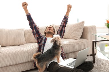 mutlu genç adam köpeğiyle oturma odasında exults