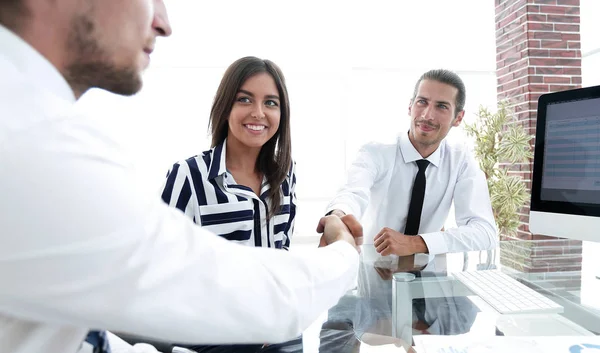 Män skakar hand och ler medan de sitter vid skrivbordet — Stockfoto