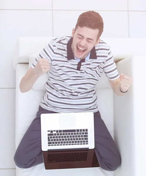 Vue du haut. jubilant jeune homme avec ordinateur portable assis sur le canapé — Photo