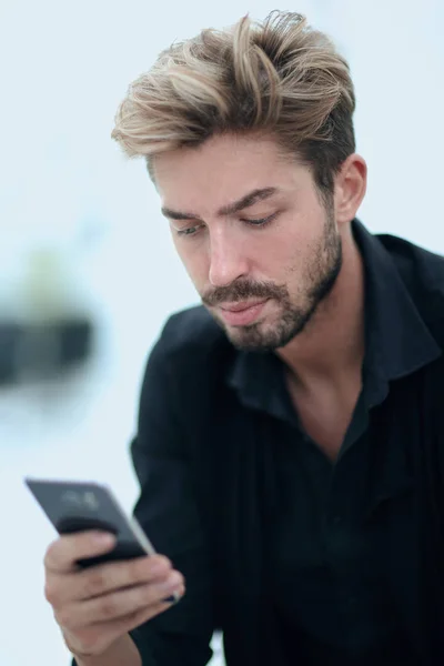 一个时髦的大胡子男性坐在和使用智能手机. — 图库照片