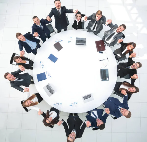 Duży zespół biznesowy siedzi przy okrągłym stole i podnosi ręce do góry — Zdjęcie stockowe