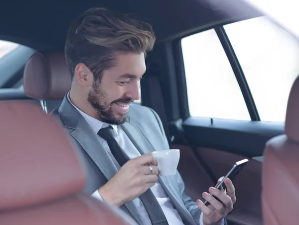 Homme d'affaires buvant du café en voiture avec téléphone à la main — Photo