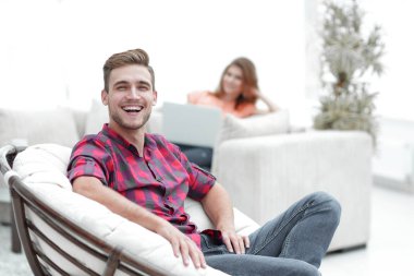 Bulanık arka planda büyük bir sandalyede oturan mutlu genç adam.