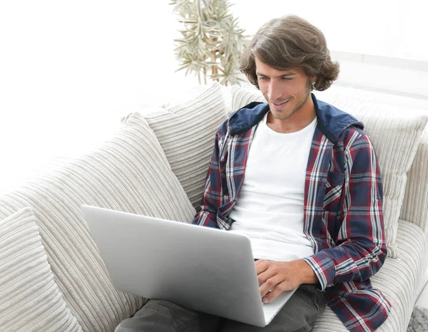 Young man working on laptop sitting on couch — Stock Photo, Image