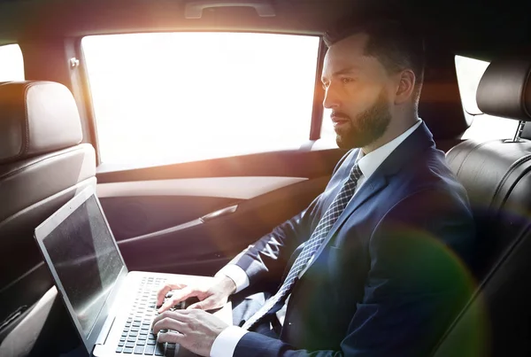 Uomo d'affari che utilizza un computer portatile nel sedile posteriore di una macchina — Foto Stock