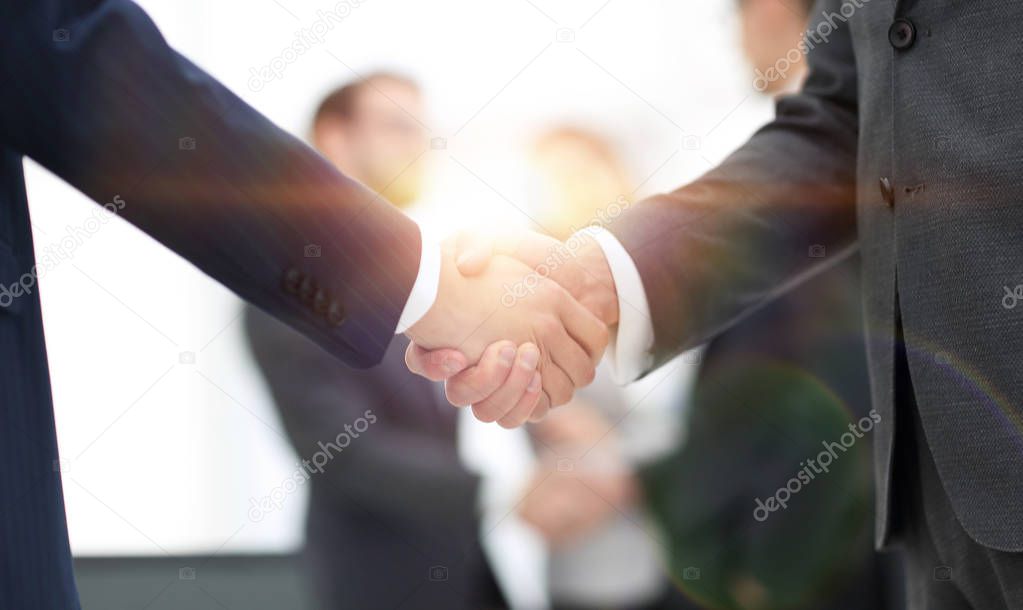 Two businessmen shaking hands with colleagues  on background.