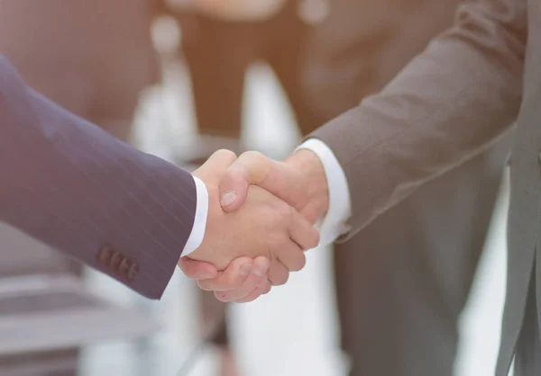 Dos hombres de negocios estrechando la mano con sus colegas de fondo. — Foto de Stock