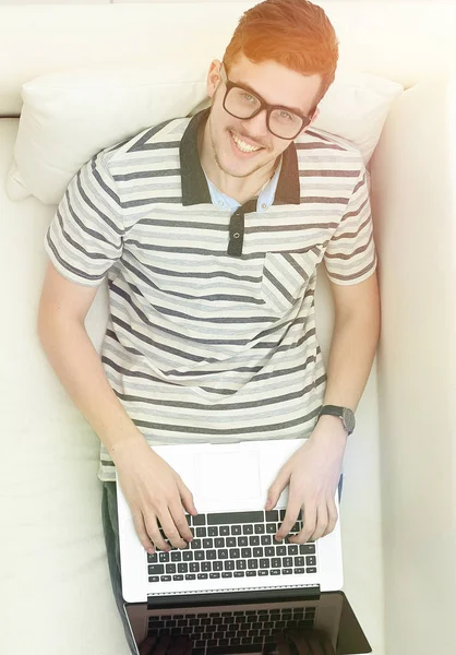 Ο σύγχρονος άνθρωπος που δουλεύει σε ένα φορητό υπολογιστή που κάθεται στον καναπέ — Φωτογραφία Αρχείου