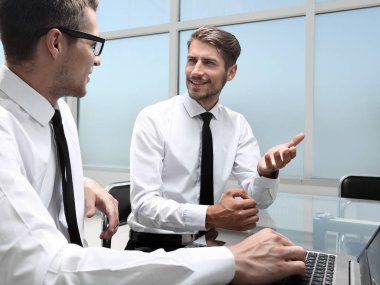 Genç ofis çalışanı gülümsüyor, iş arkadaşları arka grupta çalışıyor.