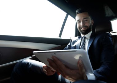 bir arabanın arka koltuğunda çalışma ve bir tablet kullanarak iş adamı