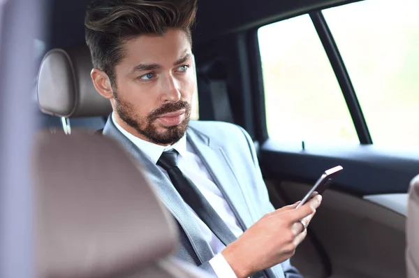 Uomo in giacca e cravatta seduto in auto e leggere messaggi su smartphone — Foto Stock