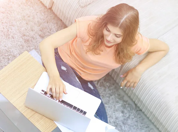 Студентка, що працює на ноутбуці, сидить на килимі біля дивана . — стокове фото