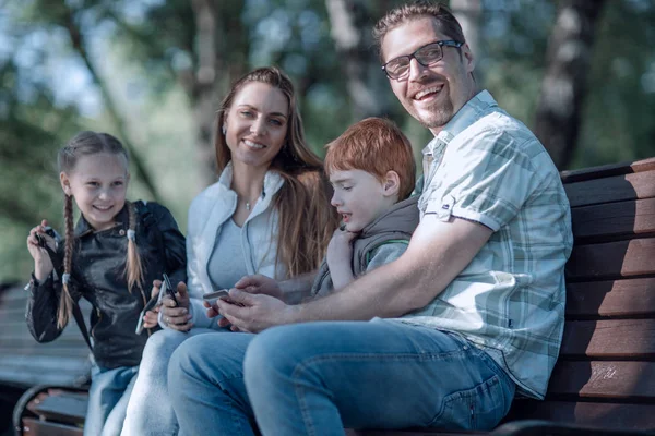 Familia feliz sentado en el banco en el parque de verano —  Fotos de Stock