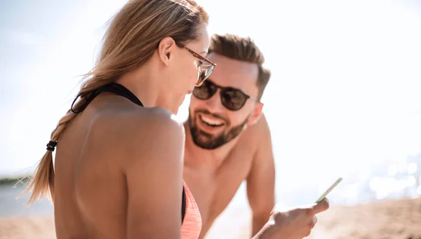 Lächelndes Paar beim Stöbern auf Fotos am Strand — Stockfoto