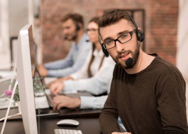 adam bir parlak ofisindeki bilgisayarlar tarafından oturan kulaklık ile