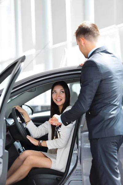 Jovem mulher recebe a chave e sorrindo, sentado em um carro novo no showroom . — Fotografia de Stock