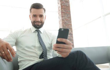 bir akıllı telefon tutarak ve kameraya bakarak işadamı