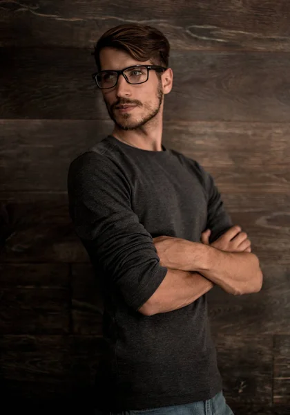 Hipster guy wearing glasses with his arms crossed on a dark back — Stock Photo, Image