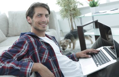 gülümseyen adam kanepede yakın katta oturan bir dizüstü bilgisayar ile