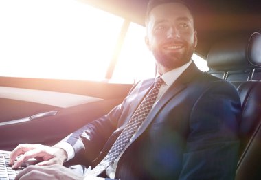 bir arabanın arka koltuğunda oturan dizüstü bilgisayar ile işadamı