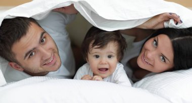 mutlu bir aile kameraya bakarken bir yorgan altında poz