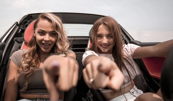 Duas namoradas felizes sentadas em um carro e apontando para você — Fotografia de Stock