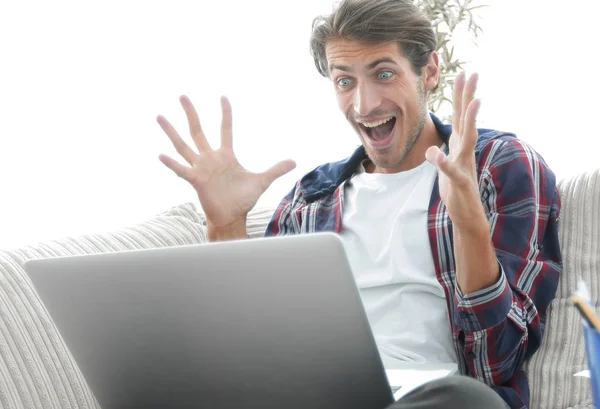 Jovem surpreso com laptop sentado no sofá — Fotografia de Stock