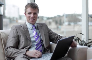 Laptop ile çalışma ofis lobisinde oturan genç işadamı