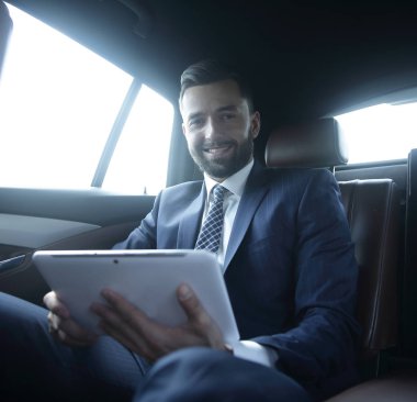 bir arabanın arka koltuğunda oturan bir dijital tablet ile işadamı