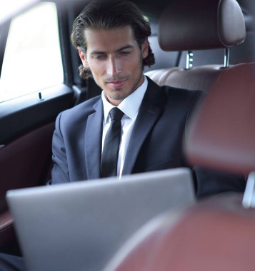 Adam arabada otururken dizüstü bilgisayarla çalışıyor.